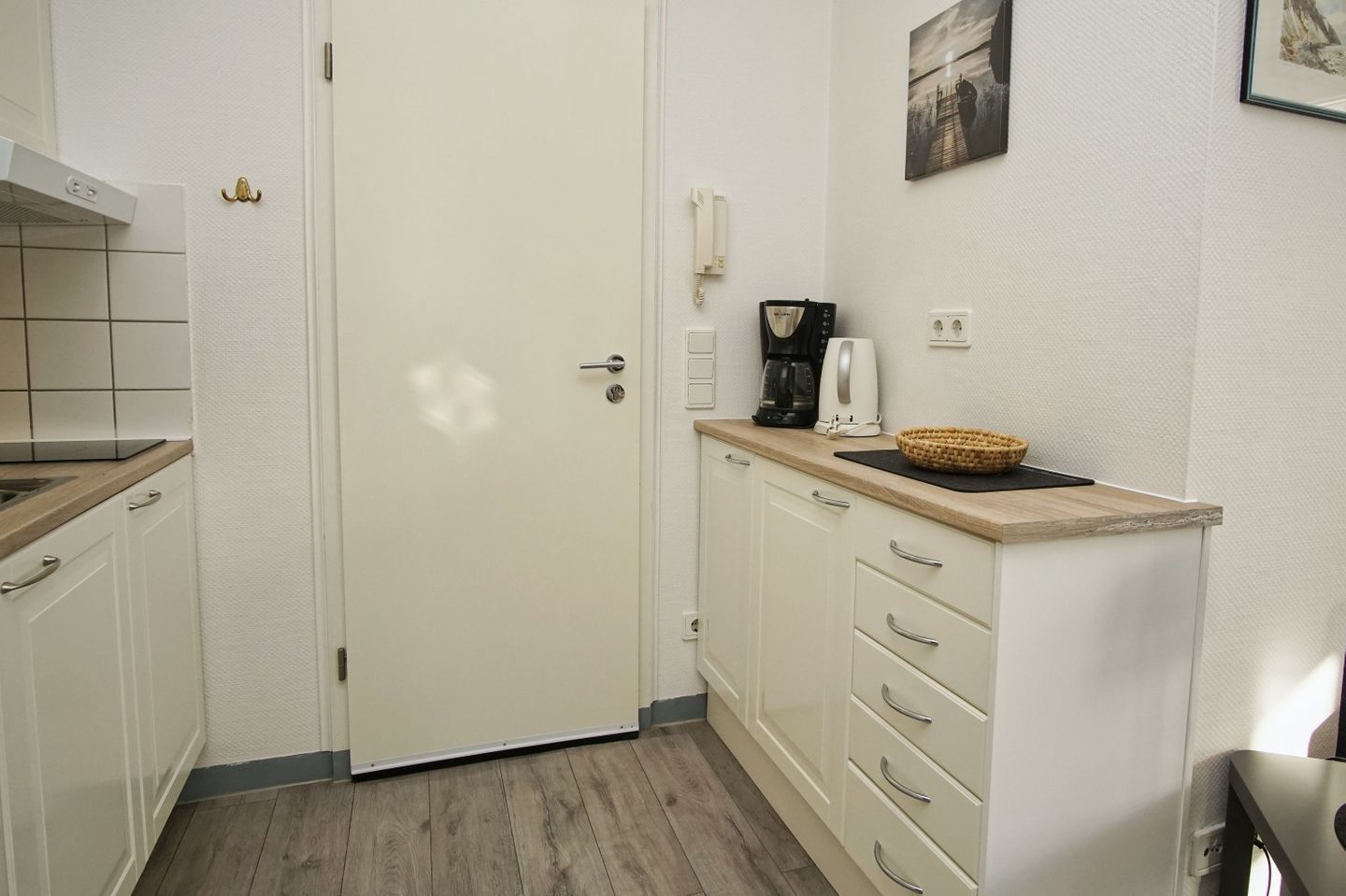 Una cocina compacta con armarios blancos, una encimera de madera, una cafetera y una cesta.
