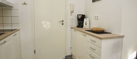 Una cocina compacta con armarios blancos, una encimera de madera, una cafetera y una cesta.