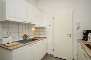 A compact kitchen with white cabinets, a wooden countertop, a sink, a toaster, and a coffee maker.
