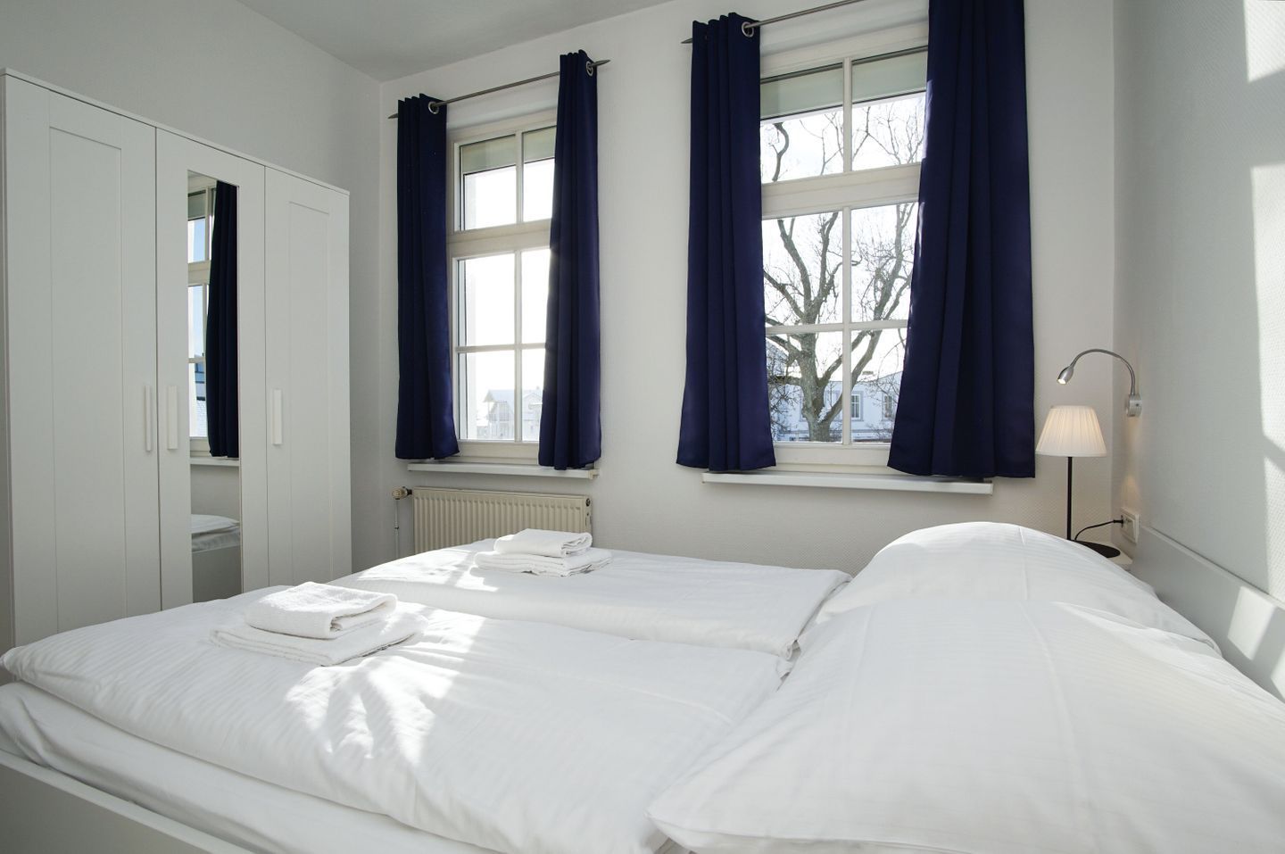Un dormitorio con cama, mesita de noche, lámpara y ventana con cortinas.