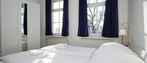 Un dormitorio con cama, mesita de noche, lámpara y ventana con cortinas.