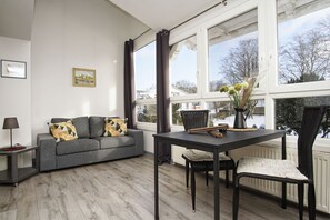 A modern living room with a grey sofa, a dining table with chairs, and a large window with a view of a snowy landscape. - im Zentrum Gelegene 2-raum-wohnung - Haus Rugier Fewo 03 - Haus Rugier (Göhren)