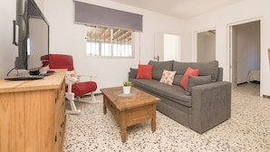 A living room with a wooden desk, red chair, grey sofa, and a television.