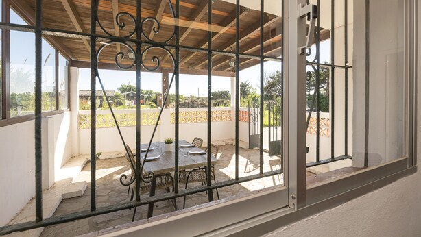 A covered patio area with a table and chairs, a view of the surrounding landscape, and a metal railing.