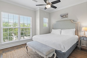 Une chambre à coucher avec un grand lit, un banc, un ventilateur de plafond et une fenêtre avec des stores.