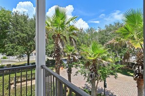 A balcony with a view of a landscaped garden featuring palm trees and a paved walkway.