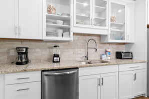 A modern kitchen with white cabinets, a granite countertop, a dishwasher, a coffee maker, a blender, a toaster, and a stainless steel sink. - 🌊Walk to Beach-Great Location-4BR Pet Friendly Beachwaves Driftwood🌊 (Miramar Beach)