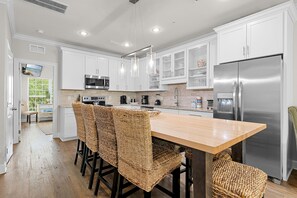A modern kitchen with white cabinets, stainless steel appliances, a wooden island with wicker chairs, and a large refrigerator. - 🌊Walk to Beach-Great Location-4BR Pet Friendly Beachwaves Driftwood🌊 (Miramar Beach)