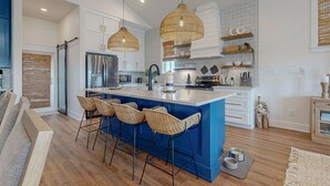 Une cuisine moderne dotée d’un îlot central, de tabourets de bar, de luminaires suspendus en osier et de meubles de rangement blancs.