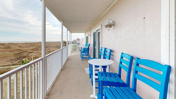 A balcony with blue chairs and a table, overlooking a barren landscape. - Gulf Views, Walk to Sandfest, Shared Pools, Boardwalk to the Beach (Port Aransas)
