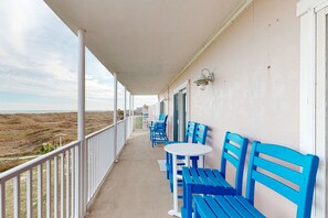 A balcony with blue chairs and a table, overlooking a barren landscape. - Gulf Views, Walk to Sandfest, Shared Pools, Boardwalk to the Beach (Port Aransas)