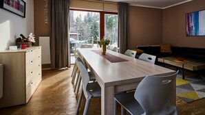 A modern dining area with a wooden table, white chairs, and a view of a snowy landscape through large windows.