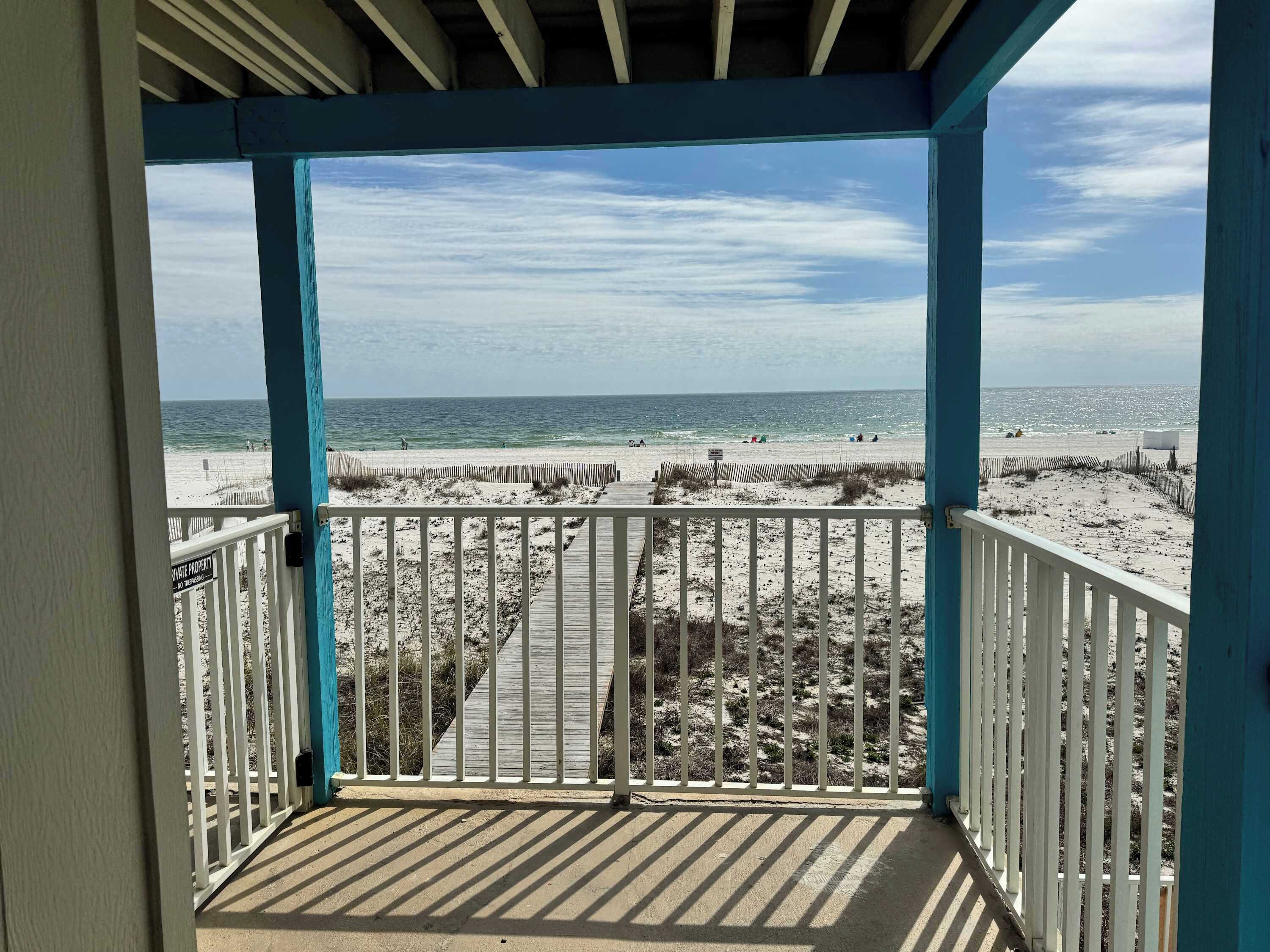 A beach view from a covered balcony with a wooden deck and white railings.