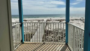 A beach view from a covered balcony with a wooden deck and white railings. - Sundial 1C -- Beachfront Complex. Beautiful condo just steps to the beach! (Gulf Shores)