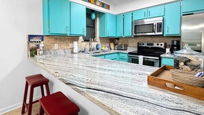 A kitchen with teal cabinets, a granite countertop, and stainless steel appliances. - Sundial 1C -- Beachfront Complex. Beautiful condo just steps to the beach! (Gulf Shores)