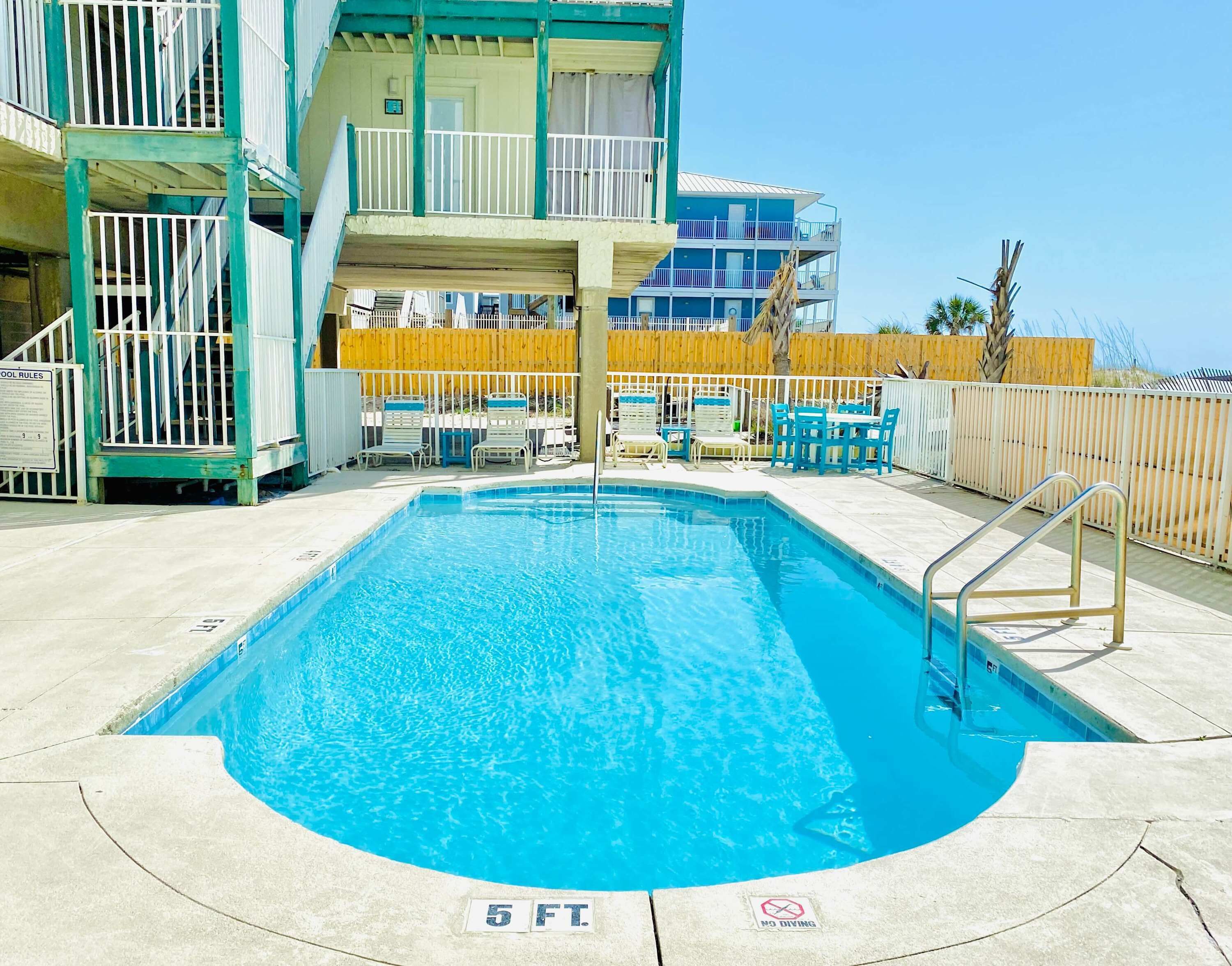 Una piscina con un indicador de profundidad de 5 pies, un letrero que prohíbe los clavados y una valla de madera al fondo.