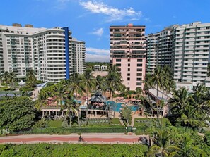 Experience the tropical ambiance of our hotel complex, surrounded by lush gardens and palm trees, with a swimming pool and lounge chairs.
