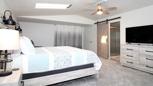 A bedroom with a bed, a TV, a ceiling fan, and a sliding door to a bathroom. - Caddy Shack 2- Charming 3-bedroom totally remodeled with AC and WiFi in Montrose (Montrose)