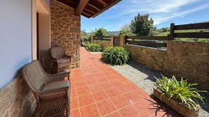 Un patio cubierto con mobiliario de mimbre, paredes de piedra y vistas a un paisaje rural.