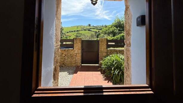 Un vano de puerta que da a un patio con pared de piedra, una verja y vistas a colinas ondulantes.