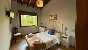 Un dormitorio con una cama grande, una ventana con vistas a la vegetación, techo de madera y una mesita de noche con lámpara.
