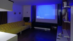 Ein Wohnzimmer mit einem gelben Sofa, einem flachbildfernseher an der Wand und einem Holzregal mit Dekoration.