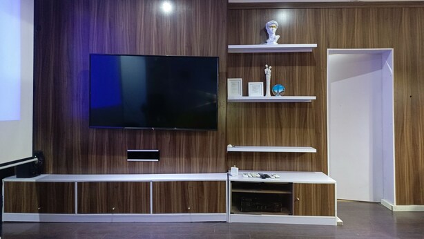 Ein modernes Wohnzimmer mit einem flachbildfernseher, der an einer Holzwand montiert ist, einer eingebauten Unterhaltungseinheit mit Regalen und einer Tür rechts.