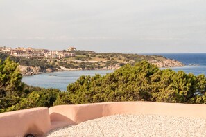 A coastal view with a building complex, a rocky shoreline, and dense greenery.