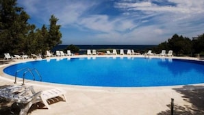 En klar, blå swimmingpool med liggestole og udsigt til havet.