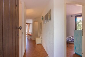 A hallway with a wooden door, a small cabinet, and a bed with a blue and white patterned bedspread.