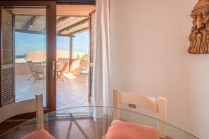 A glass table with chairs, a view of the terrace, and a wooden sculpture.