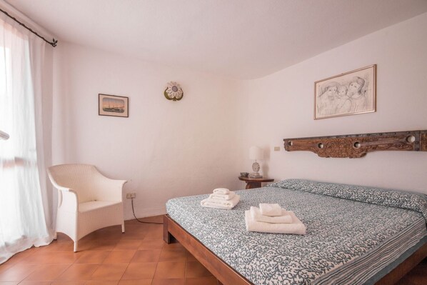 A bedroom with a bed, a chair, a nightstand, and a wall-mounted artwork.