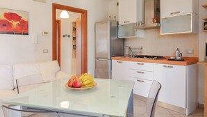 A modern kitchen with a refrigerator, stove, and white cabinets. A glass table with fruit is in the dining area. - GuestHost - Arezzo Equestrian Centre-Apt W/ Private Parking! (Arezzo)