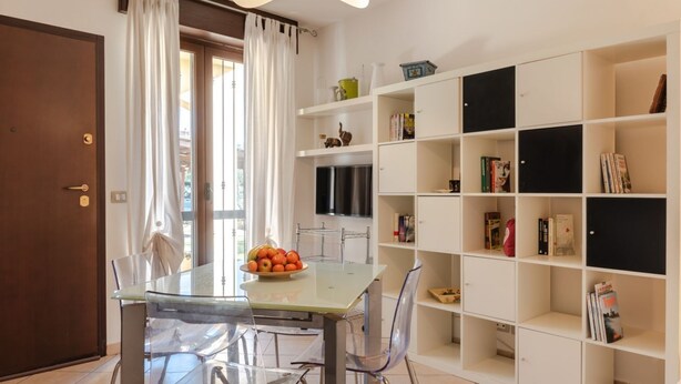 A dining area with a glass table and chairs, a fruit bowl, a bookshelf, and a TV. - GuestHost - Arezzo Equestrian Centre-Apt W/ Private Parking! (Arezzo)