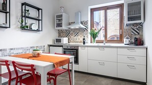 A kitchen with white cabinets, a microwave, an oven, a window with a view, and a table with chairs. - GuestHost - Palazzo dei Normanni & Ballarò Roomy Modern Apt x9 (Palermo)