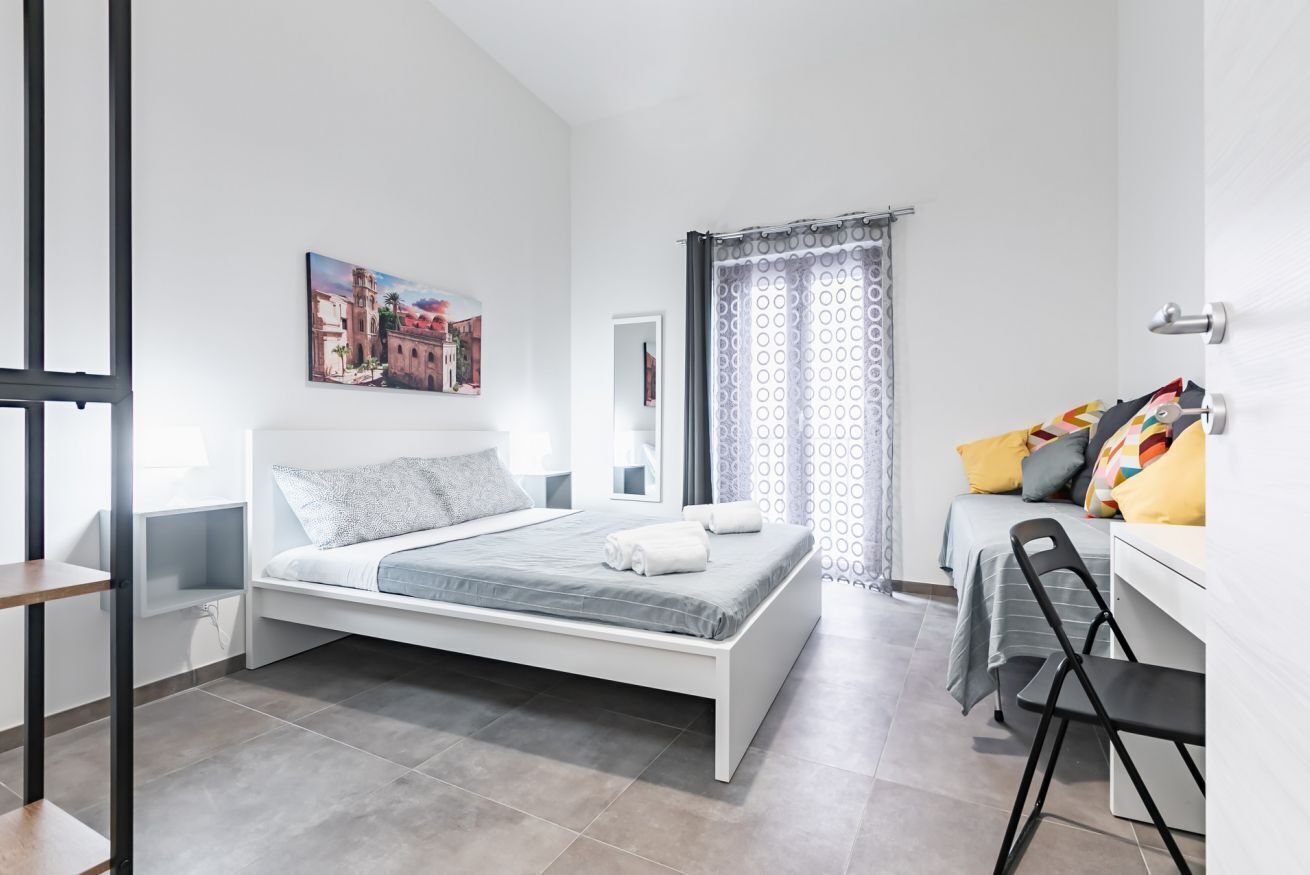 Une chambre à coucher moderne avec un lit, un bureau, une chaise, une fenêtre et un rideau.
