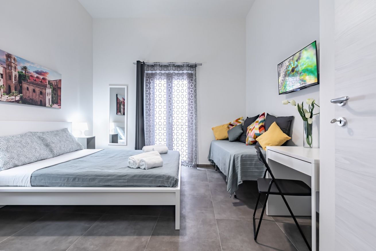 Une chambre d’hôtel moderne équipée d’un lit, d’un bureau, d’une chaise, d’une télévision et d’une fenêtre avec des rideaux à motifs.