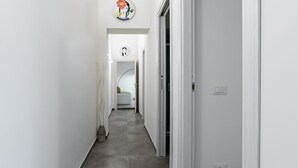 A narrow hallway with a door on the right, a light switch, and a wall-mounted clock. - GuestHost - Palazzo dei Normanni & Ballarò Roomy Modern Apt x9 (Palermo)