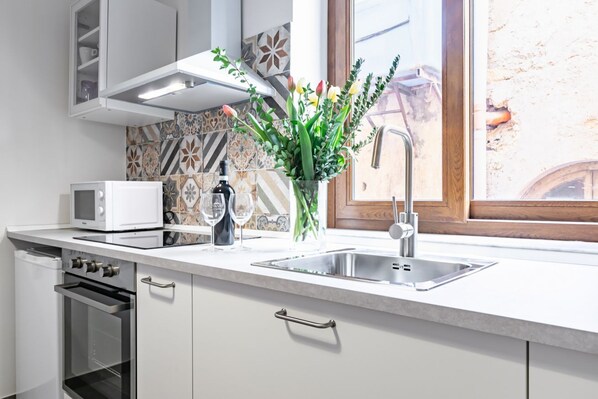 A modern kitchen with a microwave, oven, sink, and decorative vase with flowers.