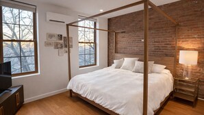 Ein Schlafzimmer mit Himmelbett, Backsteinwand und großen Fenstern.