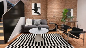 Ein modernes Wohnzimmer mit grauem Sofa, schwarz-weiß kariertem Teppich, rundem Couchtisch und einer schwarzen Metalltreppe.