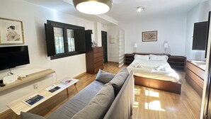 A modern hotel room with a sofa, a bed, a TV, and a desk with a lamp. - Infantes Street, Center of Seville (Sevilla)