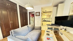 A living room with a sofa, a TV, and a small table with magazines. - Infantes Street, Center of Seville (Sevilla)