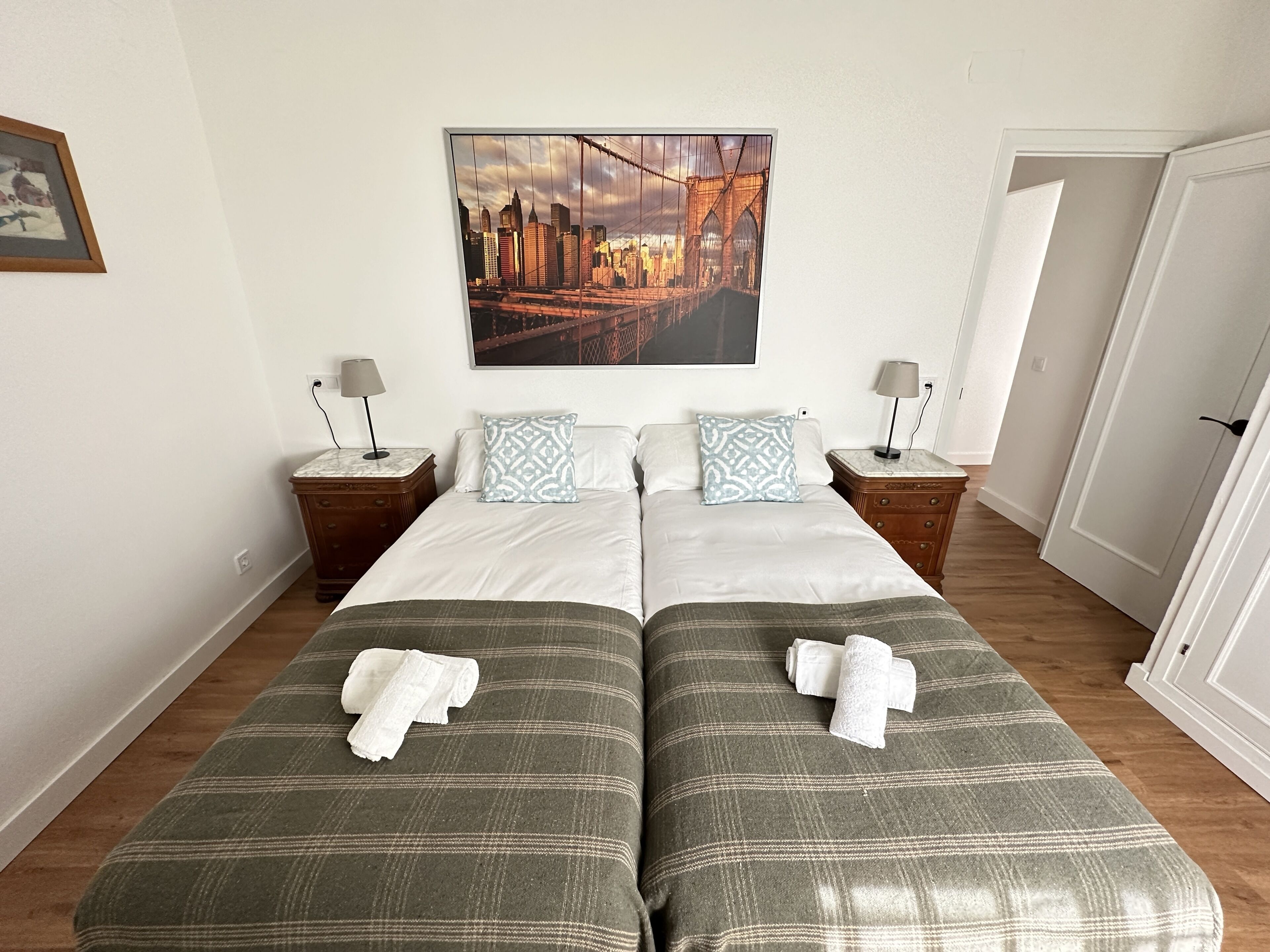 A double bed with two pillows, a nightstand with a lamp, and a framed picture on the wall.