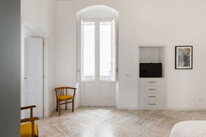 Une chambre avec une armoire blanche, un téléviseur, un tableau encadré et une chaise.