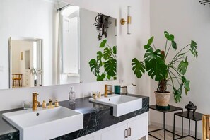 Une salle de bain moderne avec deux vasques, un grand miroir et un monstera en pot.