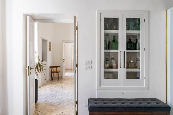 Un couloir avec un banc, une armoire à portes vitrées et une porte donnant sur une autre pièce.
