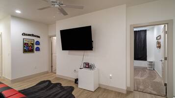 Una sala de estar con ventilador de techo, televisor montado, letrero que indica sala de juegos y un sofá rojo y negro.