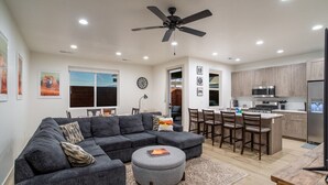 Una sala moderna con un sofá modular, un reposapiés y una zona de comedor con sillas.