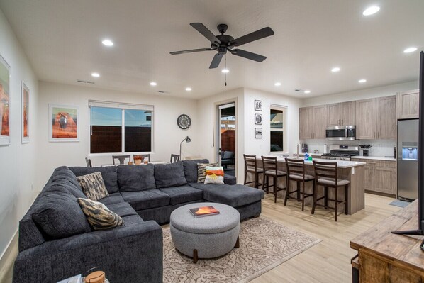A modern living room with a sectional sofa, ottoman, and dining area with chairs.